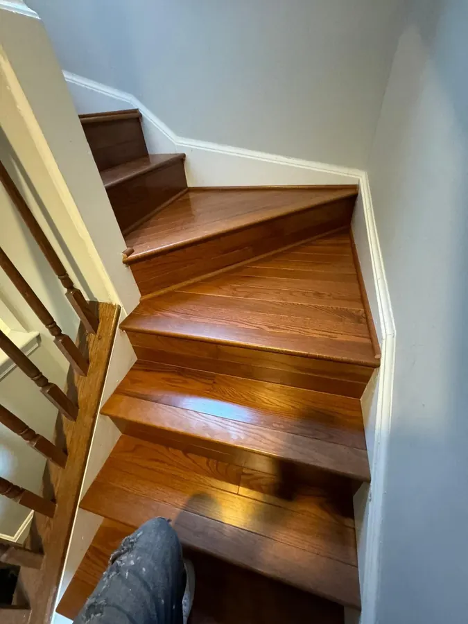 Cherry toned hardwood stairs running down past a white painted wall