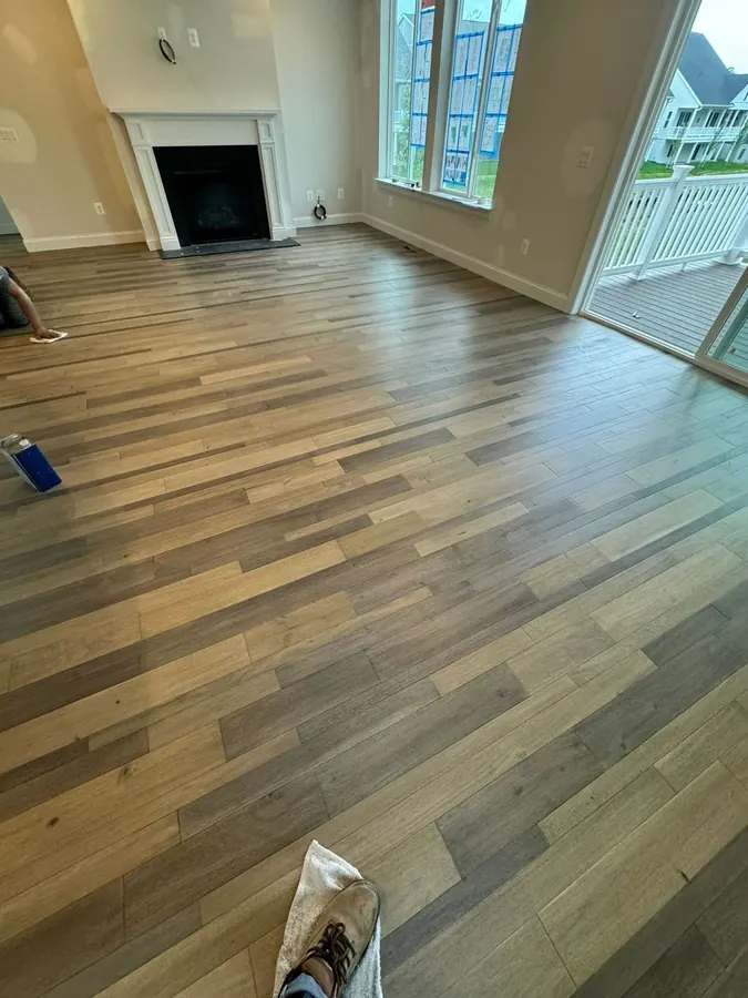 Wide plank flooring across a great room with a fireplace and tall windows