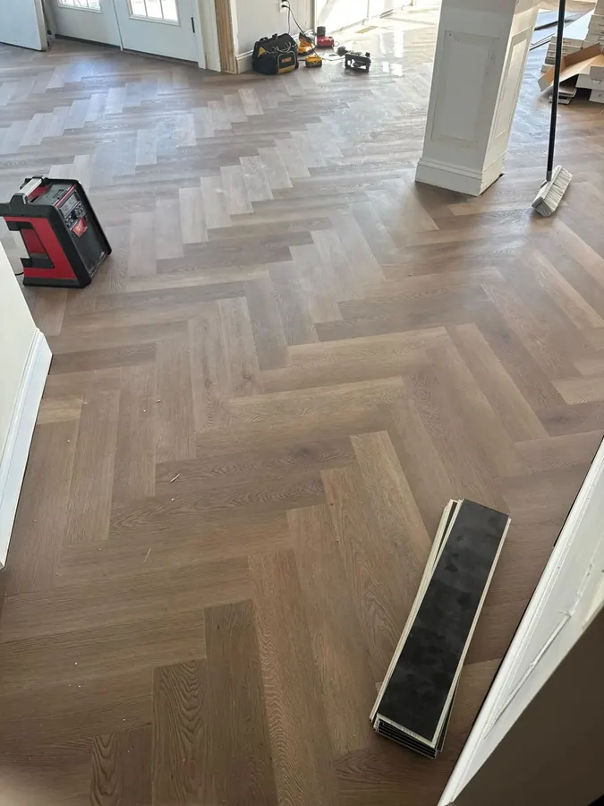 Herringbone oak across a large room with a laser level set up on the floor
