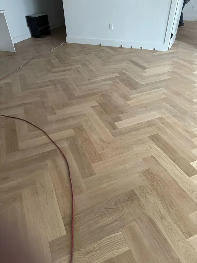 Pale oak herringbone laid across a room before the baseboard goes back on