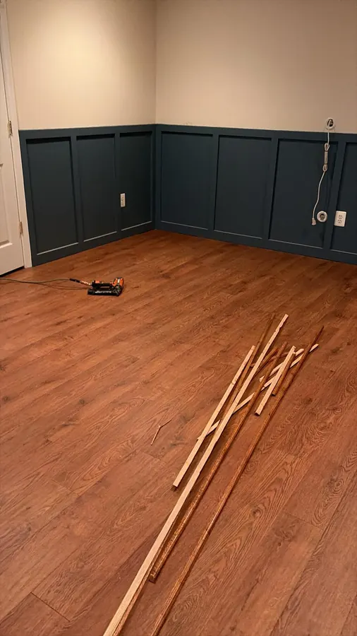 Oak toned flooring in a room with navy wainscot, trim laid out ready to fit